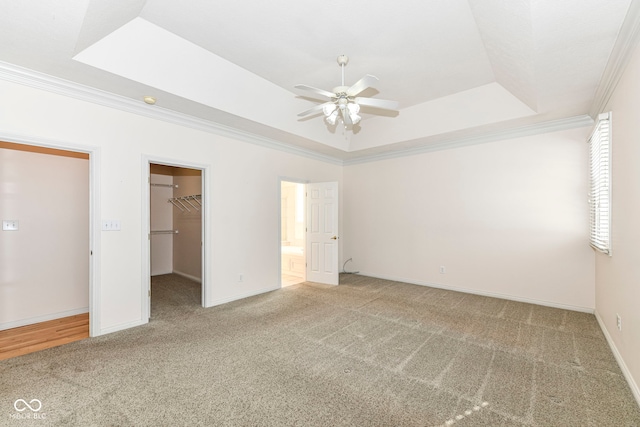 unfurnished bedroom featuring ceiling fan, a raised ceiling, a spacious closet, ornamental molding, and a closet