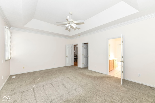 unfurnished bedroom with ensuite bathroom, ornamental molding, ceiling fan, light colored carpet, and a tray ceiling