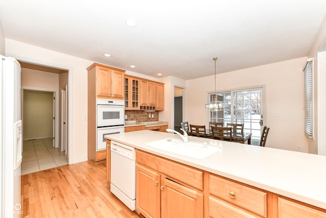 kitchen with decorative backsplash, white appliances, light wood-type flooring, pendant lighting, and sink