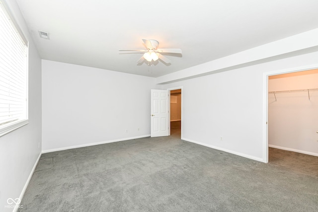 unfurnished bedroom with a spacious closet, a closet, ceiling fan, and dark colored carpet