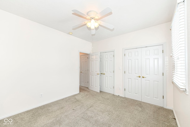 unfurnished bedroom with ceiling fan, light carpet, and two closets