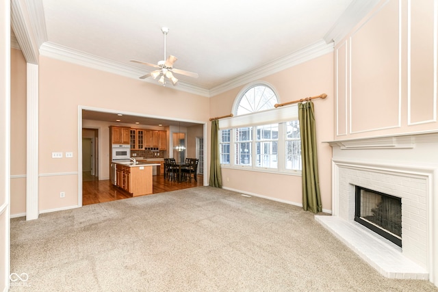 unfurnished living room with ceiling fan, light colored carpet, a fireplace, and crown molding