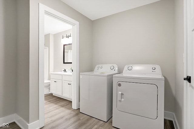 laundry area with washing machine and clothes dryer, light hardwood / wood-style flooring, and sink