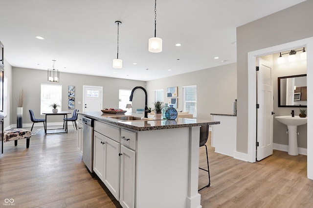 kitchen with decorative light fixtures, stainless steel appliances, a kitchen bar, a kitchen island with sink, and white cabinetry