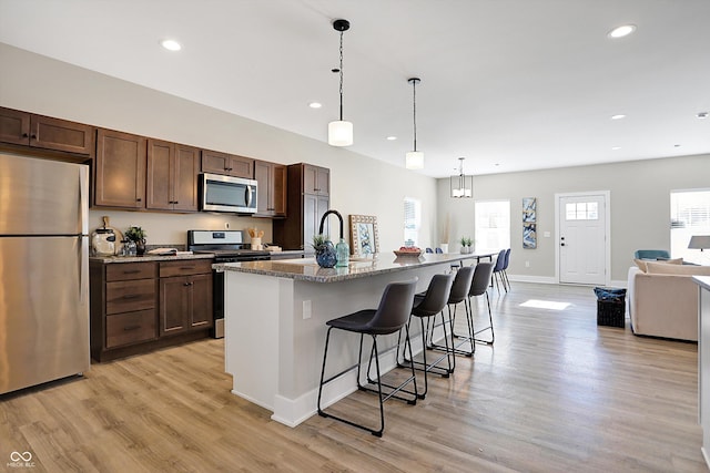 kitchen with a kitchen breakfast bar, a kitchen island with sink, stainless steel appliances, stone counters, and decorative light fixtures