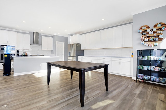 kitchen with stainless steel appliances, a kitchen island with sink, light wood-type flooring, wall chimney exhaust hood, and white cabinets