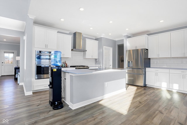 kitchen featuring white cabinetry, wall chimney range hood, stainless steel appliances, and a center island with sink