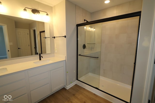 bathroom with a sink, wood finished floors, a stall shower, and double vanity