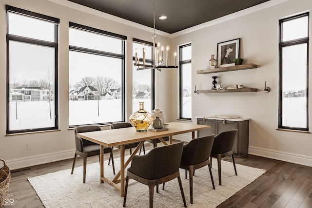 dining area with dark wood-type flooring, a chandelier, crown molding, and a healthy amount of sunlight