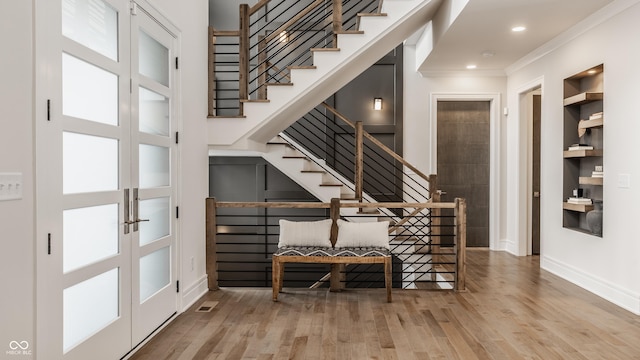 stairway featuring french doors, built in features, crown molding, and wood-type flooring