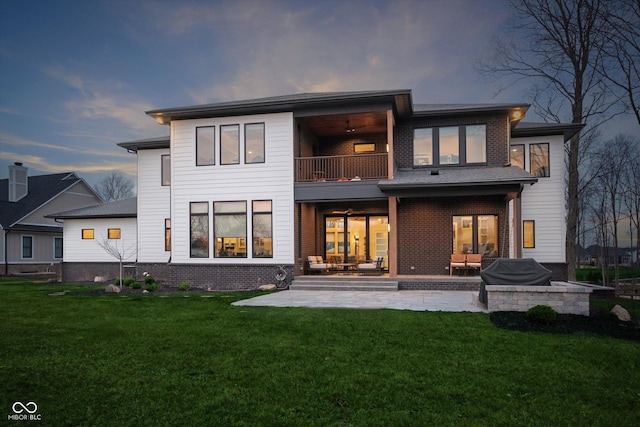 back house at dusk with a lawn, a balcony, and a patio