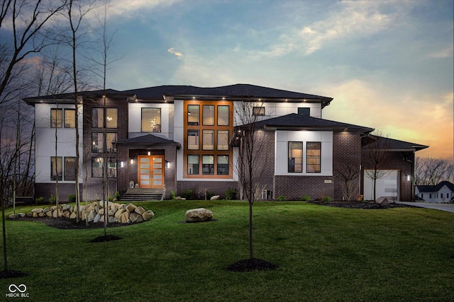 prairie-style house with a yard, brick siding, an attached garage, and driveway