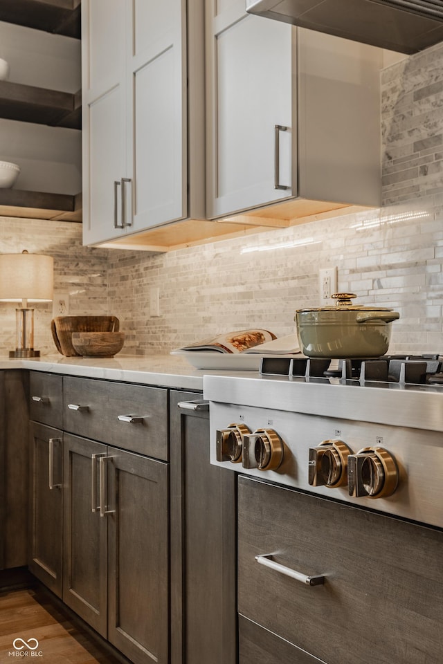 kitchen with dark hardwood / wood-style floors, tasteful backsplash, dark brown cabinets, stovetop, and range hood