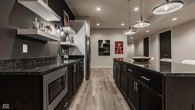 kitchen with appliances with stainless steel finishes, a center island, decorative light fixtures, dark stone countertops, and sink