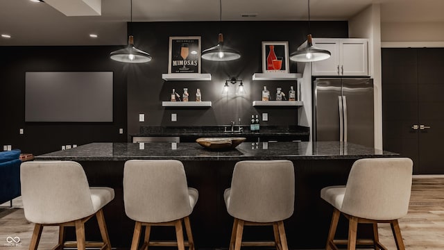 bar with pendant lighting, white cabinetry, dark stone counters, stainless steel refrigerator, and light wood-type flooring