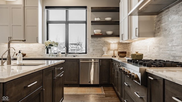 kitchen featuring tasteful backsplash, wall chimney range hood, sink, white cabinets, and light stone counters