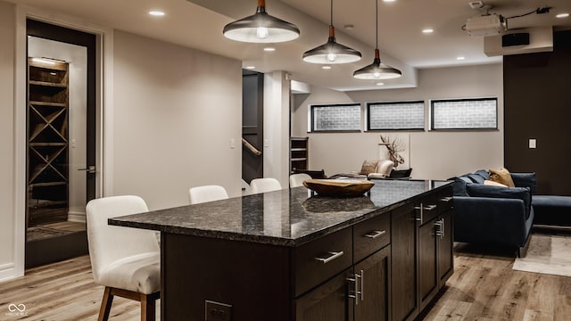 kitchen featuring pendant lighting, a center island, dark stone counters, light wood-type flooring, and a breakfast bar area