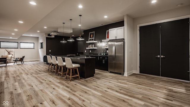 kitchen with white cabinetry, stainless steel fridge, a kitchen breakfast bar, light wood-type flooring, and a center island