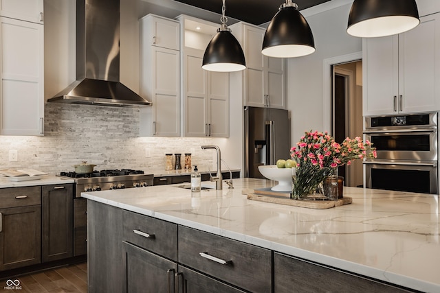 kitchen featuring pendant lighting, white cabinets, appliances with stainless steel finishes, dark wood-type flooring, and wall chimney range hood