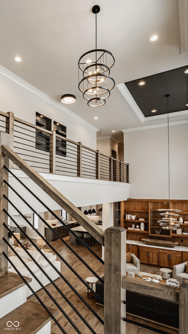 staircase featuring a raised ceiling, a notable chandelier, ornamental molding, and hardwood / wood-style floors