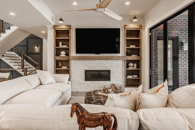 living room with ceiling fan, wood-type flooring, a stone fireplace, and built in shelves