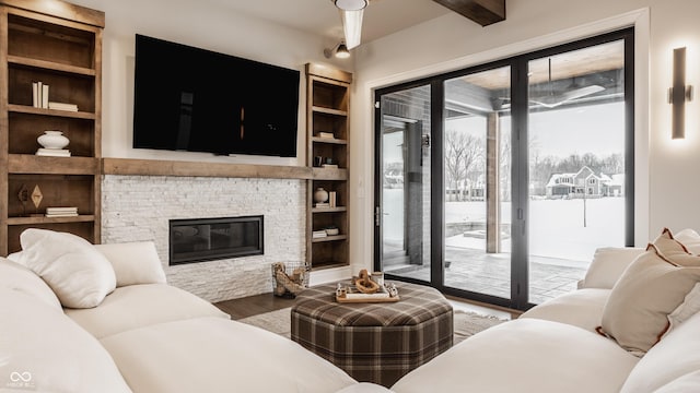 living room with wood-type flooring, built in features, beam ceiling, and a stone fireplace