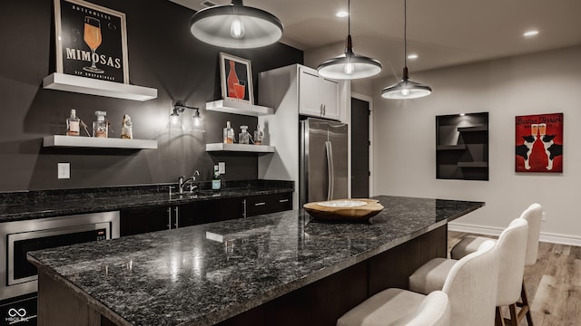 kitchen with decorative light fixtures, sink, dark stone counters, a kitchen breakfast bar, and stainless steel fridge