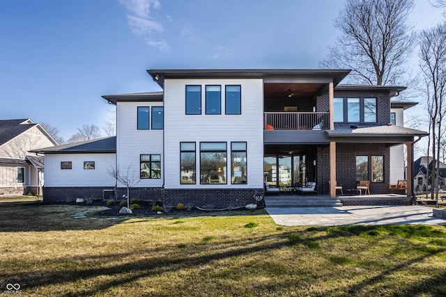 rear view of house with a lawn, a balcony, and a patio