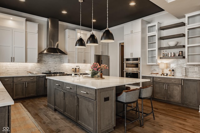 kitchen featuring backsplash, a center island with sink, stainless steel appliances, white cabinets, and wall chimney exhaust hood