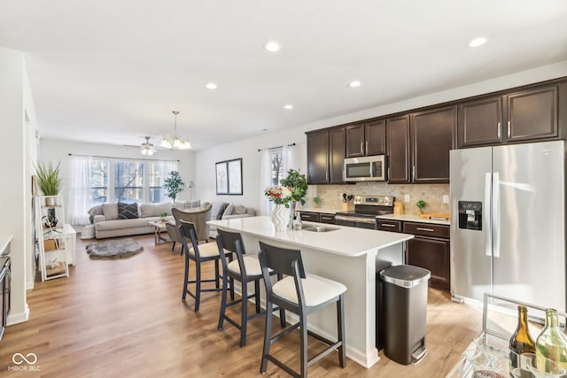 kitchen featuring hanging light fixtures, stainless steel appliances, a center island with sink, a breakfast bar, and dark brown cabinetry