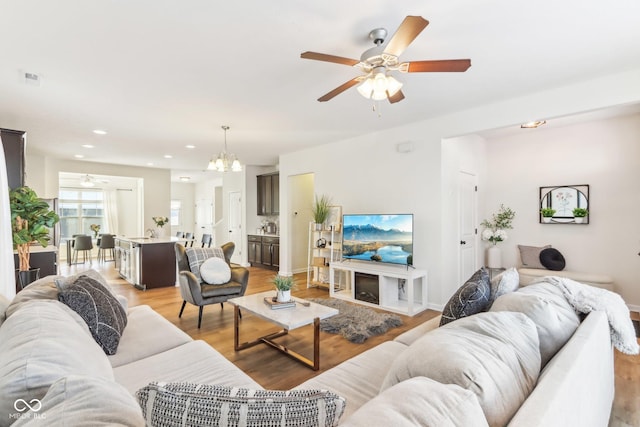 living room with ceiling fan with notable chandelier, a fireplace, and light hardwood / wood-style floors