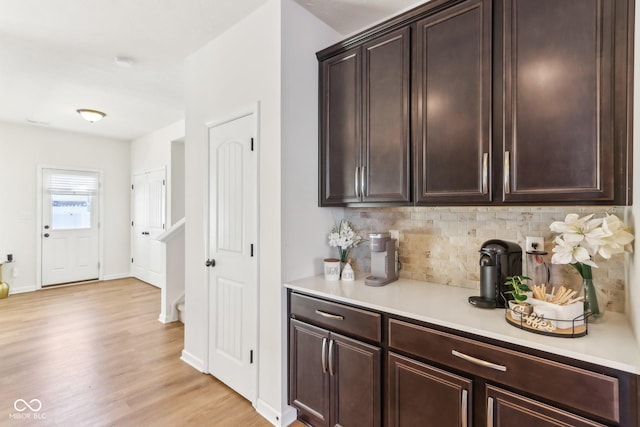 bar featuring light wood-type flooring, backsplash, and dark brown cabinetry