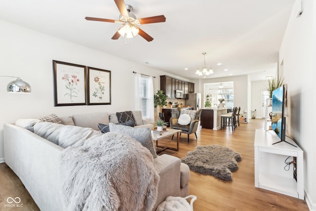 living room featuring ceiling fan with notable chandelier and light hardwood / wood-style flooring