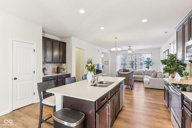 kitchen featuring a kitchen breakfast bar, a center island with sink, stainless steel appliances, sink, and ceiling fan with notable chandelier