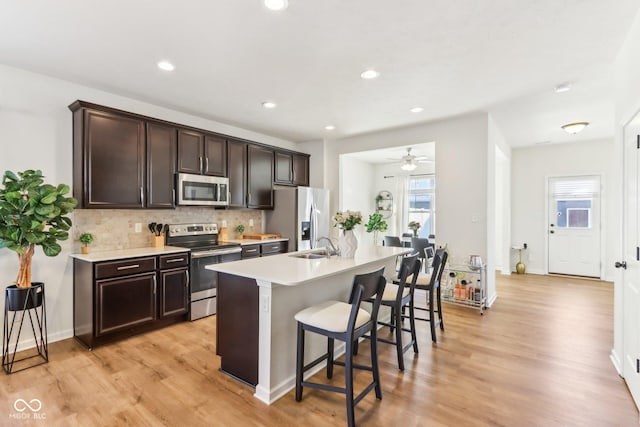 kitchen featuring stainless steel appliances, a kitchen breakfast bar, ceiling fan, an island with sink, and dark brown cabinets