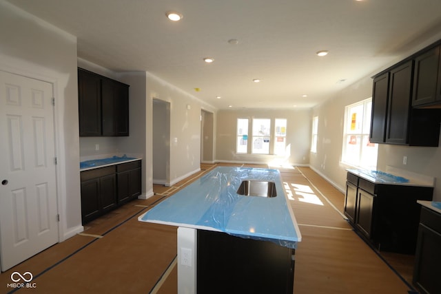 kitchen featuring a center island with sink, baseboards, recessed lighting, a sink, and open floor plan