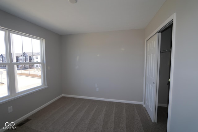 empty room featuring visible vents, dark carpet, and baseboards