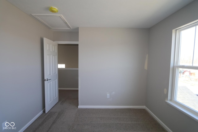 empty room with carpet flooring, attic access, and baseboards