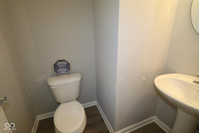 half bath with toilet, wood finished floors, baseboards, and a sink