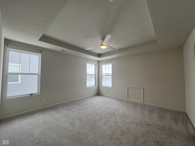 empty room with ceiling fan, a textured ceiling, carpet flooring, and a tray ceiling