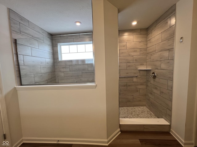 bathroom with a textured ceiling, tiled shower, and wood-type flooring