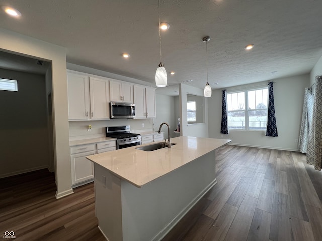 kitchen with hanging light fixtures, a kitchen island with sink, white cabinets, appliances with stainless steel finishes, and sink