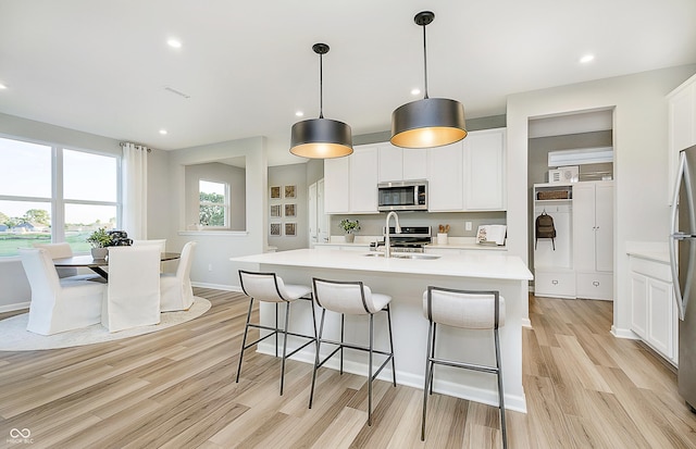 kitchen with appliances with stainless steel finishes, decorative light fixtures, white cabinetry, an island with sink, and sink