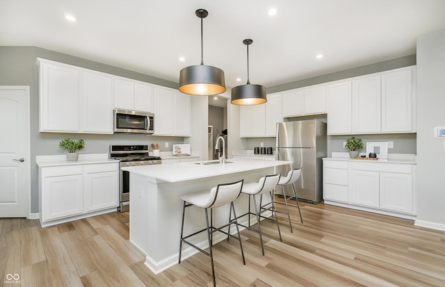 kitchen featuring pendant lighting, white cabinets, appliances with stainless steel finishes, a kitchen island with sink, and light hardwood / wood-style flooring