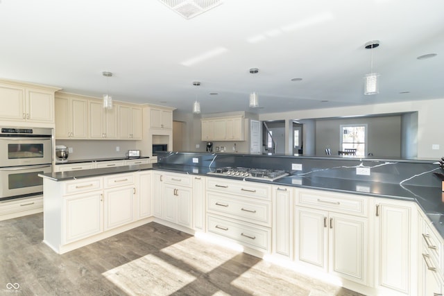 kitchen with pendant lighting, appliances with stainless steel finishes, kitchen peninsula, cream cabinets, and light hardwood / wood-style flooring