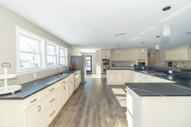 kitchen with appliances with stainless steel finishes, sink, hanging light fixtures, dark hardwood / wood-style floors, and cream cabinets