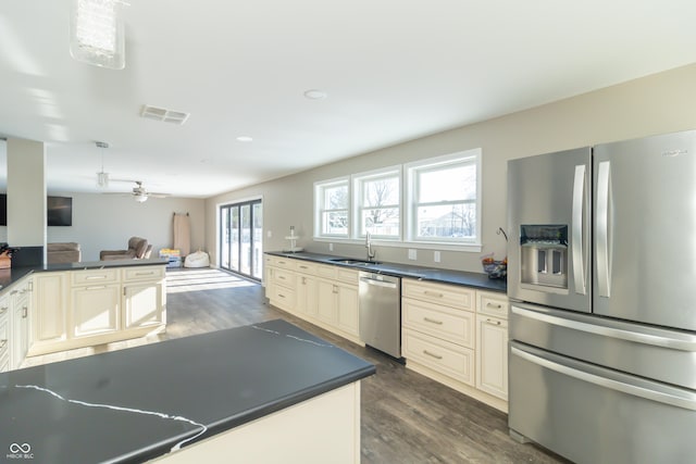 kitchen with cream cabinets, appliances with stainless steel finishes, sink, decorative light fixtures, and dark hardwood / wood-style flooring