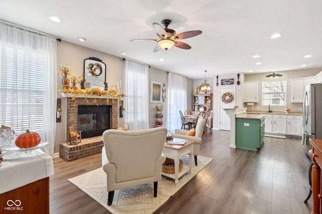 living room with ceiling fan, a brick fireplace, and dark hardwood / wood-style flooring