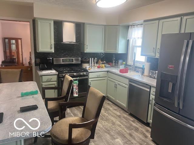 kitchen with backsplash, light wood-type flooring, appliances with stainless steel finishes, and wall chimney range hood