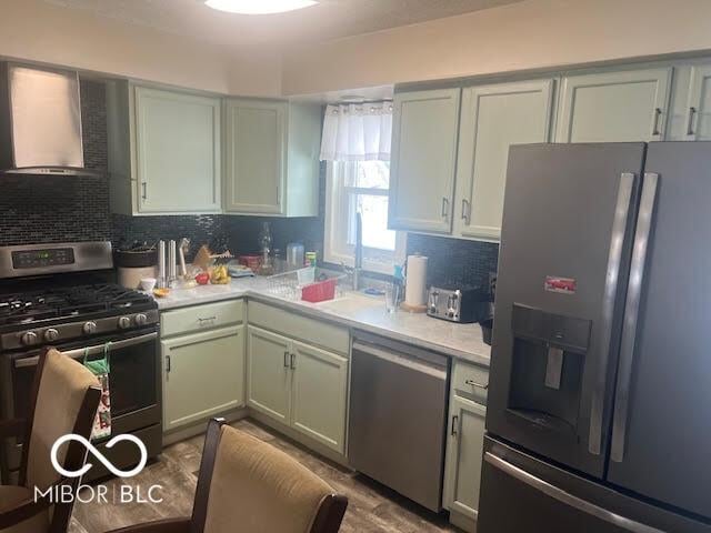 kitchen with tasteful backsplash, light wood-type flooring, appliances with stainless steel finishes, and wall chimney range hood